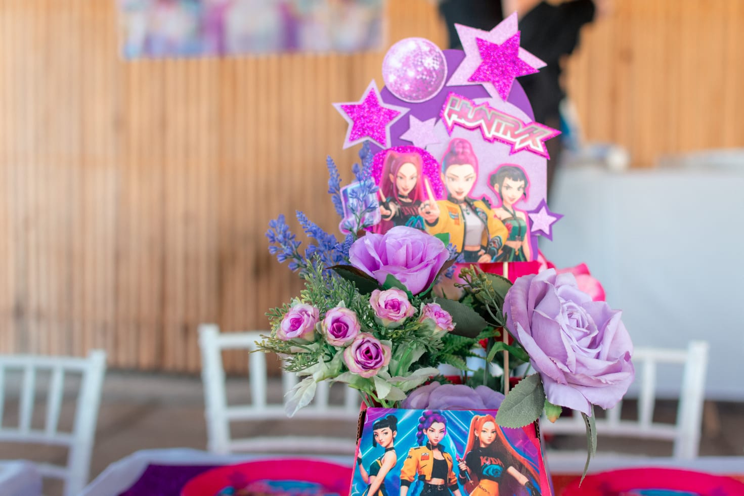 Floral table centrepiece of pink and purple roses with a pop star topper and glittery stars