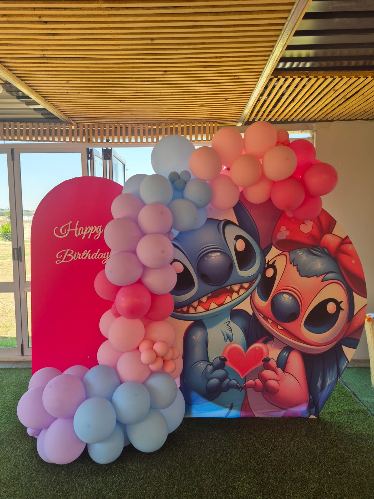 Lilo & Stitch party backdrop with Stitch and Angel holding a heart beneath a pink and baby-blue balloon arch